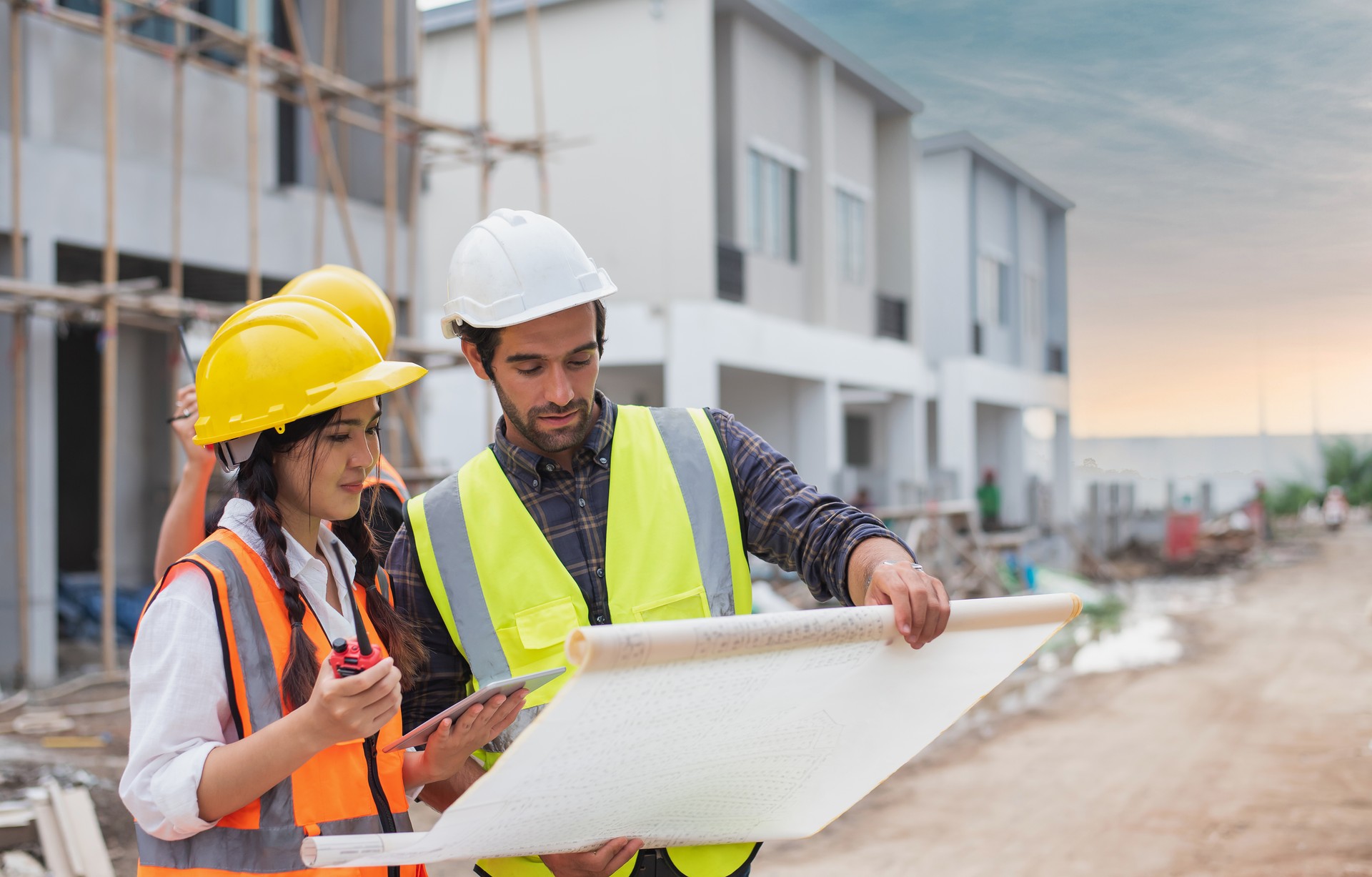 Homens caucasianos e construtores asiáticos, arquitetos e engenheiros com plano de construção e computador portátil falando sobre o local de construção